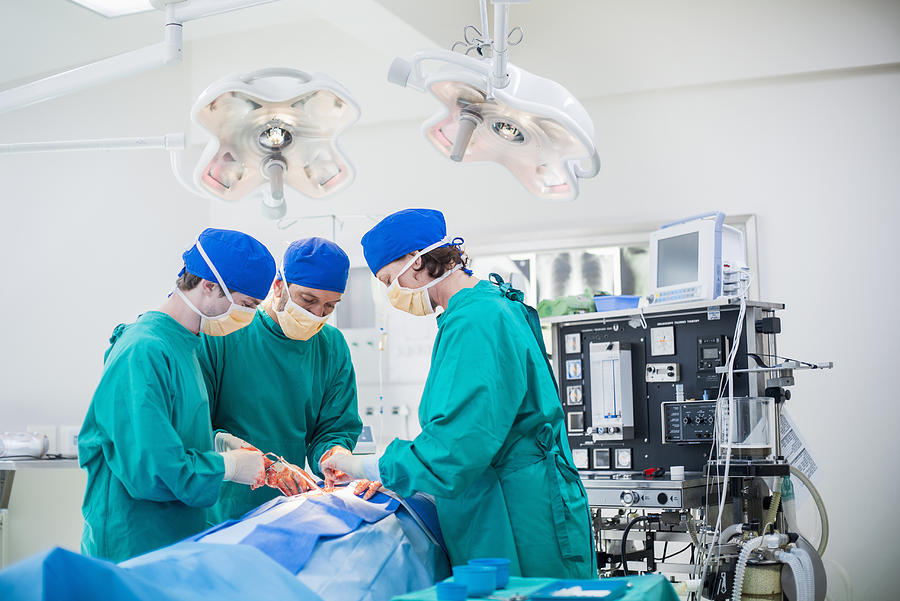 Three surgeons performing a surgery Photograph by Portra Images