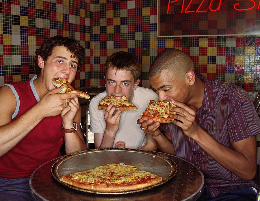 Three teenage boys (15-18) eating pizza Photograph by Tony Hopewell