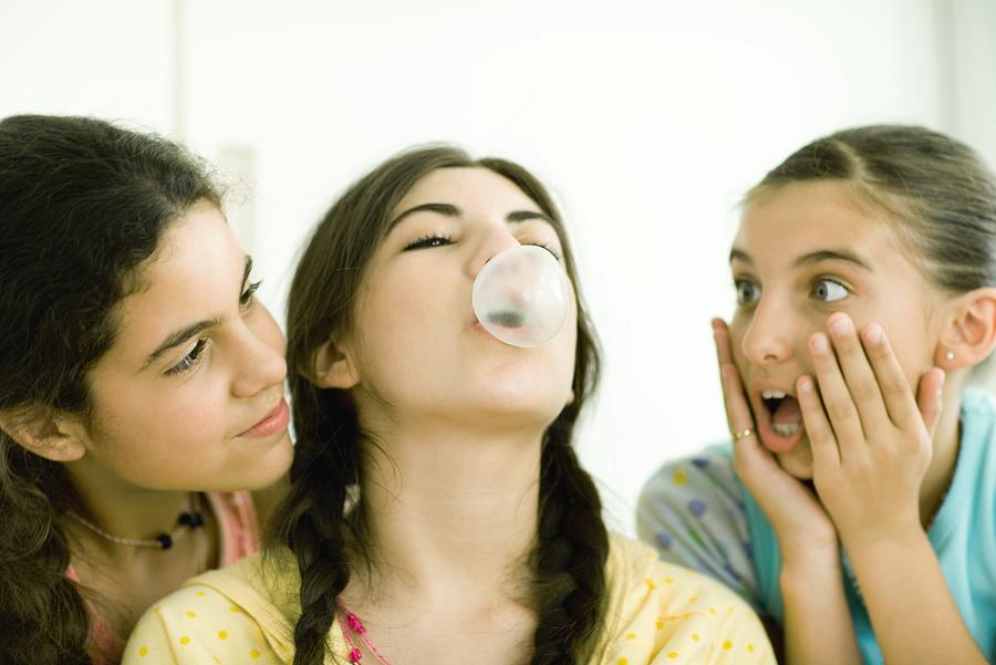 Three young female friends, one blowing bubble while others watch Photograph by PhotoAlto/Laurence Mouton