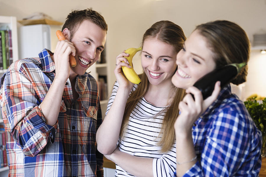 Three young people having fun using fruit as telephones Photograph by Suedhang