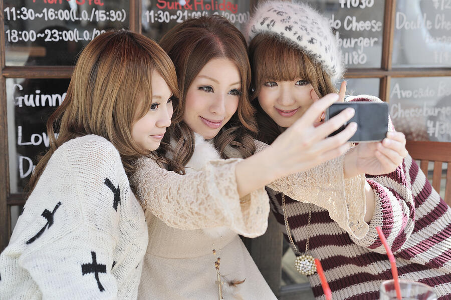 Three young women are taking photo on smartphone Photograph by Yagi Studio