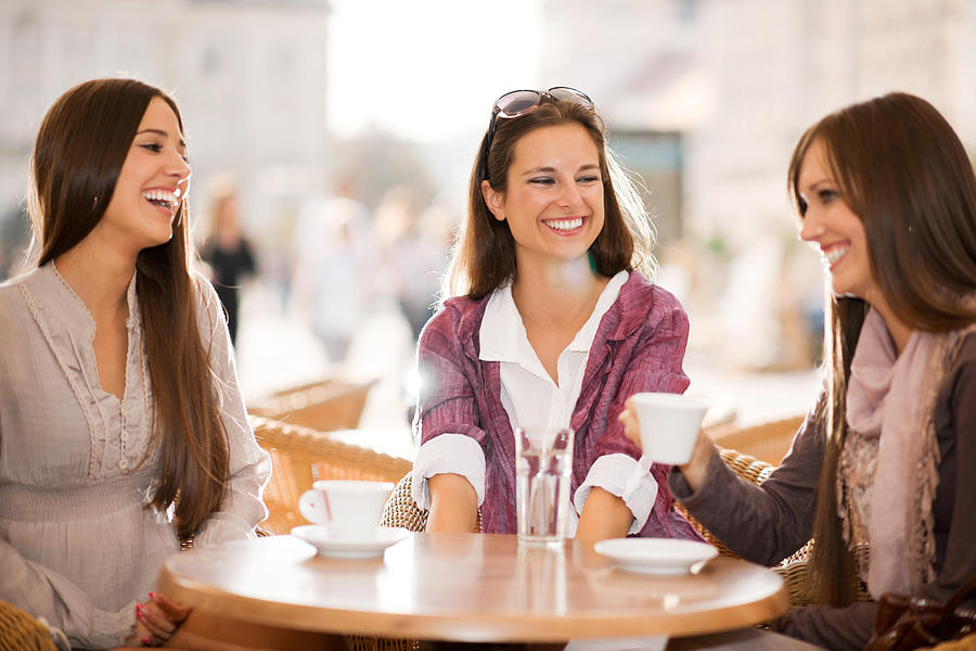 Three young women drinking coffee in a cafe. Photograph by Skynesher