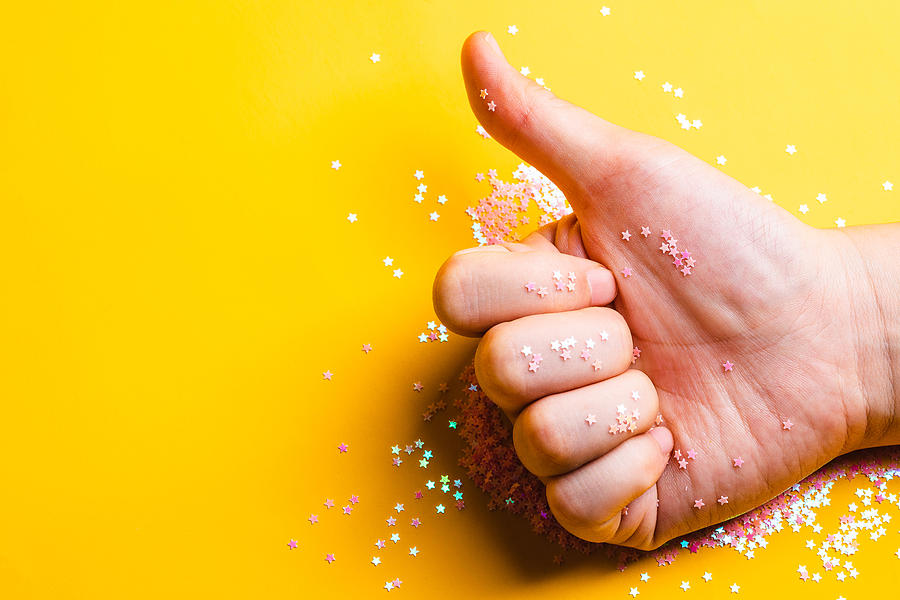 Thumb up with glittering litter stars against yellow background Photograph by Kilito Chan