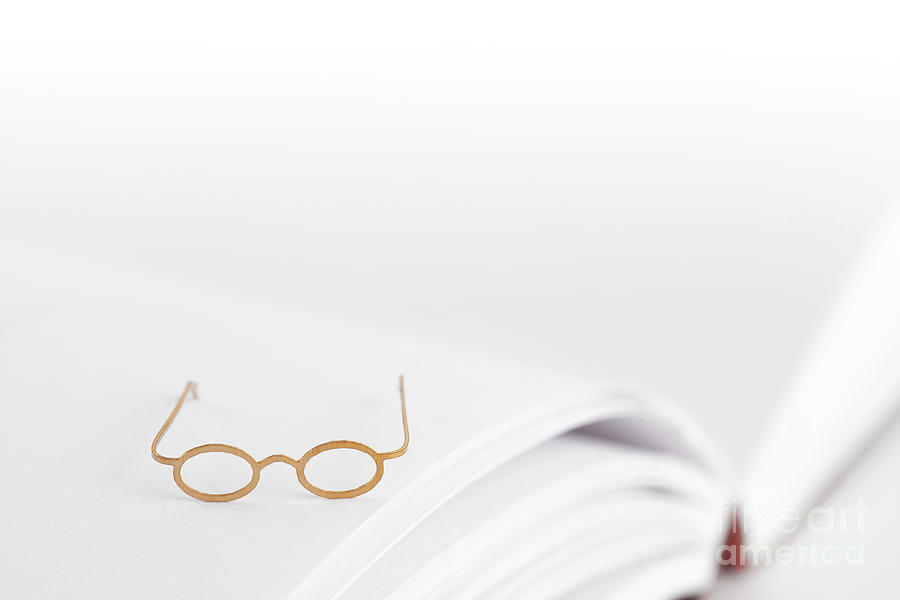 Tiny reading glasses on open book Photograph by Simon Bratt
