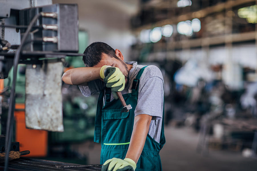 Tired guy working on a machine in factory workshop Photograph by South_agency