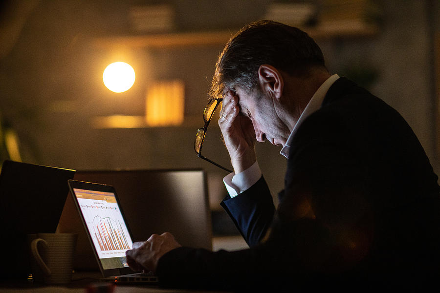 Tired man using laptop late at night in office Photograph by Miodrag Ignjatovic