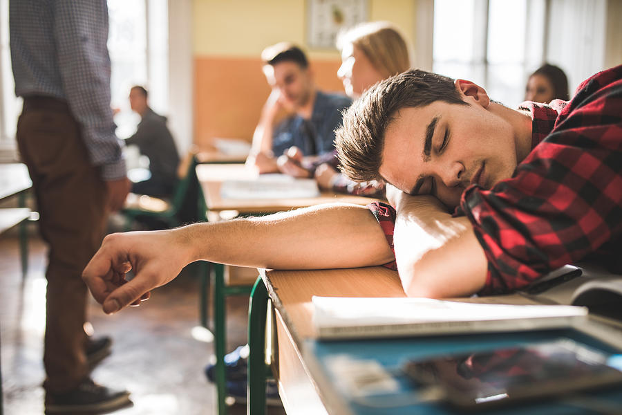 Tired teenage boy napping at school during the class. Photograph by Skynesher