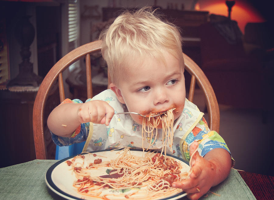 Toddler boy feeding himself spaghetti Photograph by Becki Bennett
