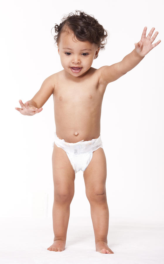Toddler girl in diapers standing on a white set. Photograph by Marcy Maloy