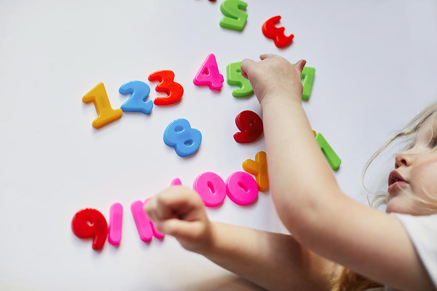 Toddler playing with magnetic letters and numbers Photograph by Sally Anscombe