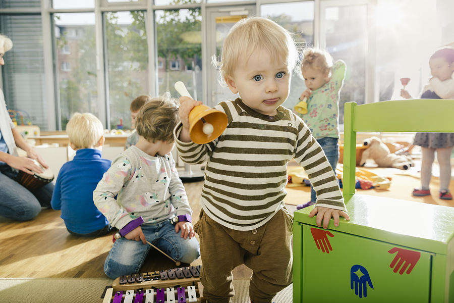 Toddler ringing a bell in music room of a kindergarten Photograph by Westend61