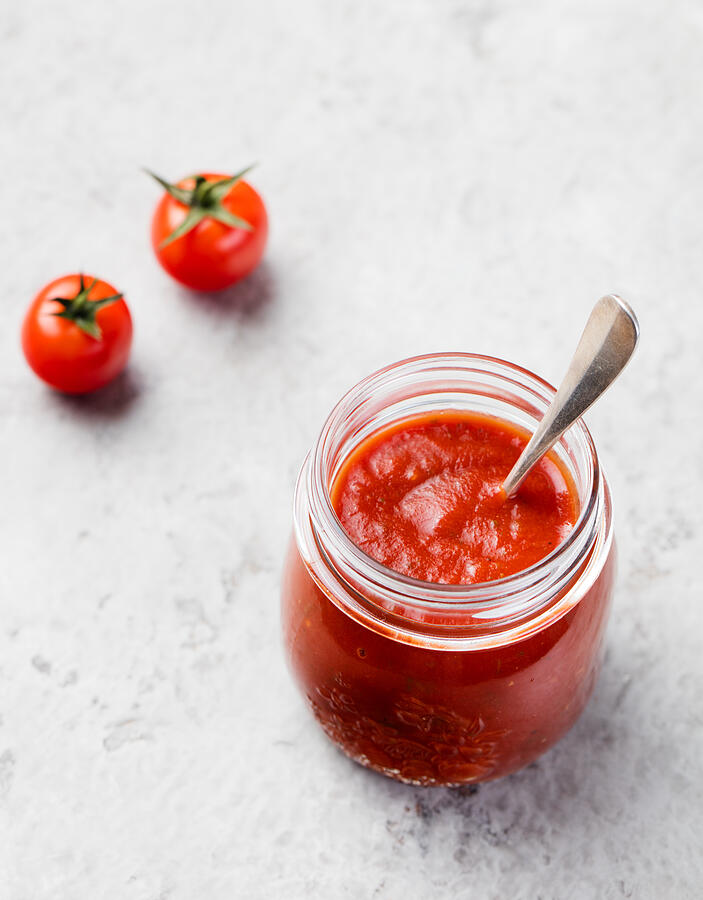 Tomato sauce in glass jar and cherry tomatoes Photograph by AnnaPustynnikova
