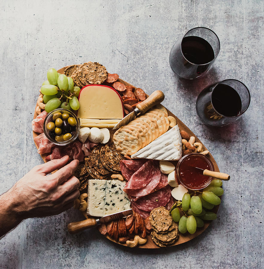 Top view of hand taking food off charcuterie board on stone counter. Photograph by Cavan Images