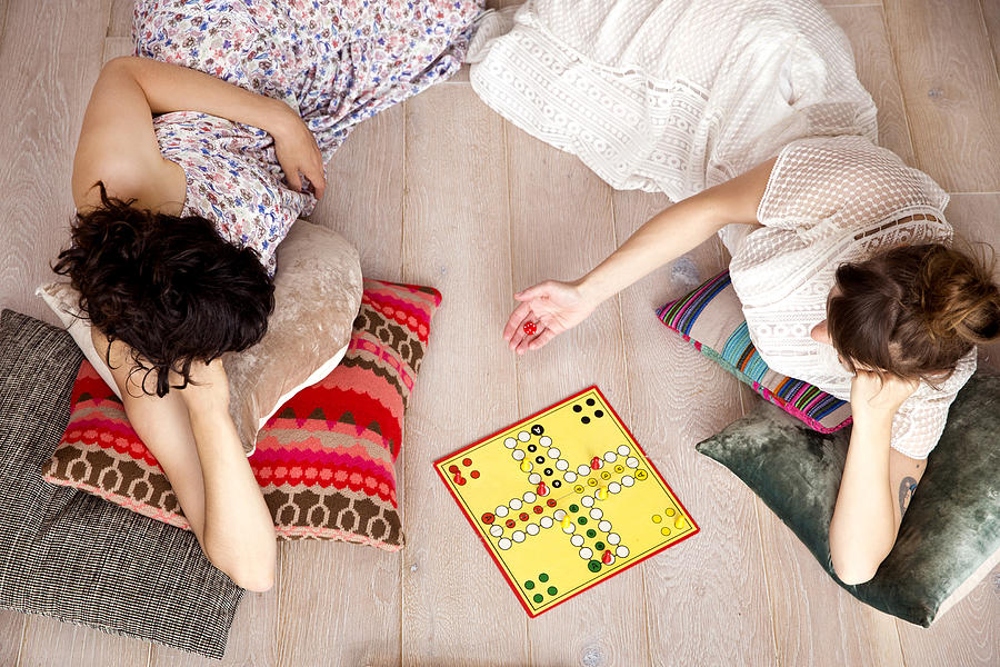 Top view of two best friends lying on the floor at home playing ludo Photograph by Westend61