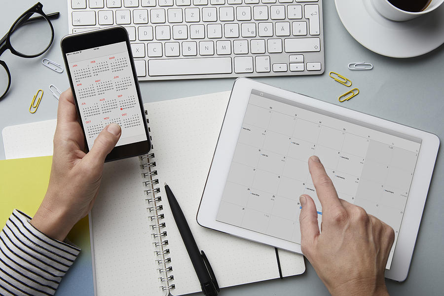 Top view of woman holding smartphone and tablet with calendar on desk Photograph by Westend61