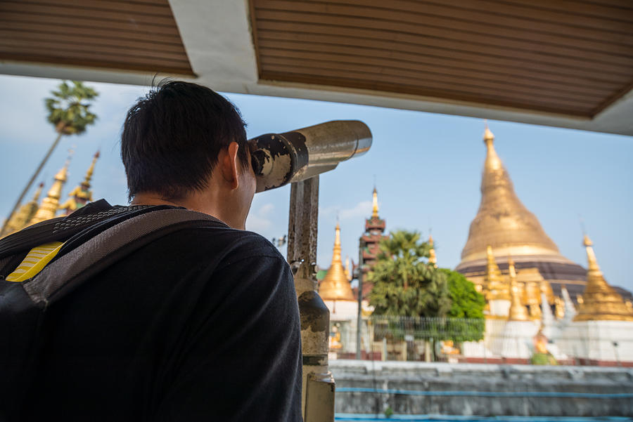 Tourist use the binoculars for looking the diamond and precious gem on the top of Shwedagon pagoda. Photograph by Boy_Anupong