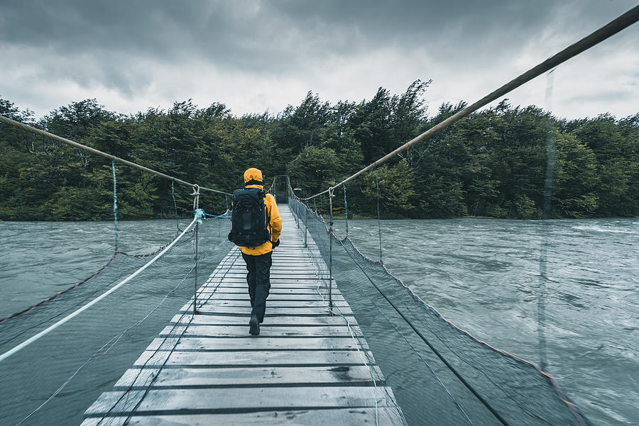 Tourist walking on a wooden bridge over a swollen river Photograph by © Marco Bottigelli