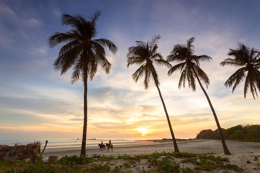 Tourists horse riding on a tropical beach at sunset, Costa Rica Photograph by Matteo Colombo