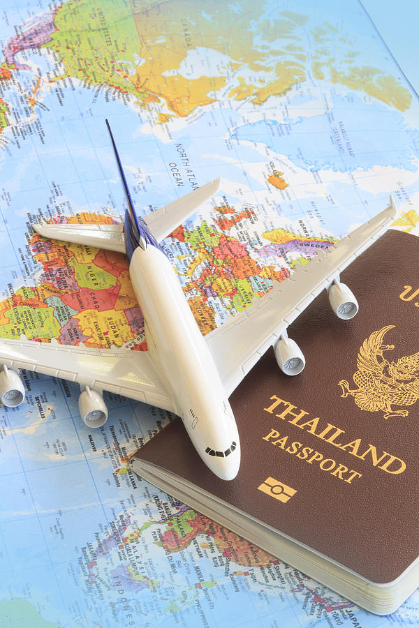 Toy plane resting on a thailand passport and world map Photograph by Keang