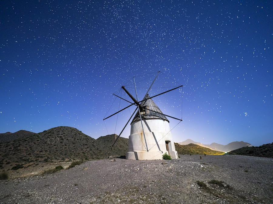 Traditional windmill among mountains in a sunny arid a night of blue sky with stars. Natural Park of Cabo de Gata - Nijar, in Almeria,  Andalucia, Spain. Photograph by Jose A. Bernat Bacete