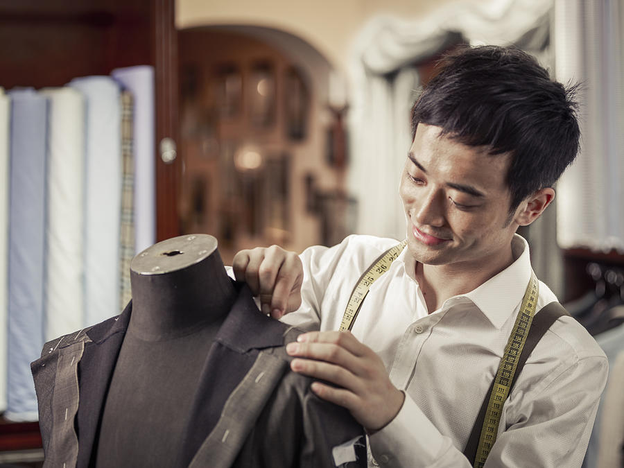 Trainee tailor pinning garment in traditional tailors shop Photograph by Rimagine Group Limited