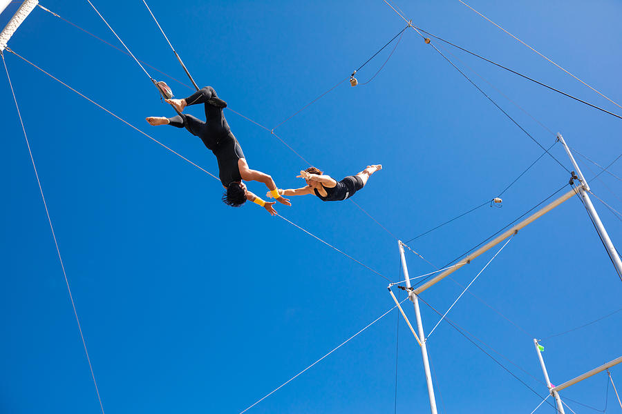 Trapeze artists flying in the blue sky Photograph by Satoshi-K