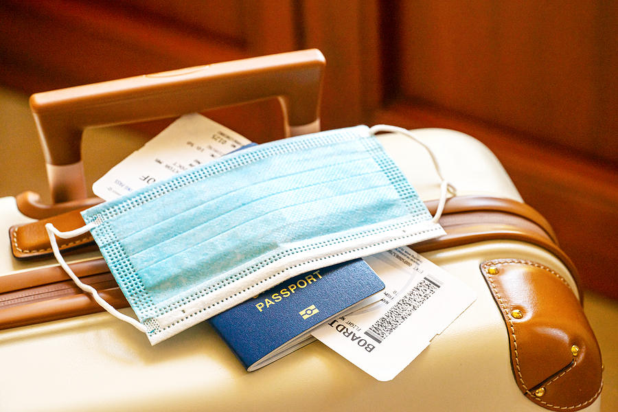 Travel suitcase or luggage, passport, air ticket and facial mask during the pandemic of Coronavirus or Covid-19.. Photograph by Iryna Veklich