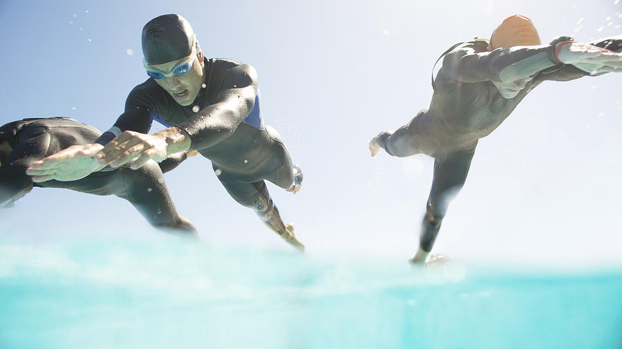Triathletes in wetsuits running into ocean Photograph by Caia Image