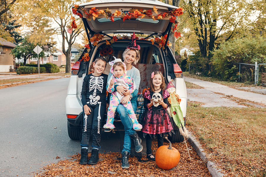 Trick or trunk. Family celebrating Halloween in trunk of car. Mother with three children kids celebrating traditional October holiday outdoors. Social distance and safe alternative celebration. Photograph by ~UserGI15613517