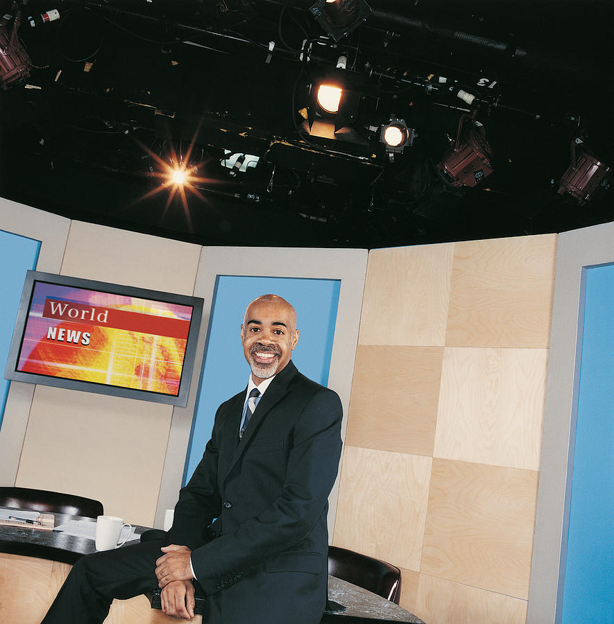 TV Presenter Sitting on a Desk in a TV Studio Photograph by Digital Vision.