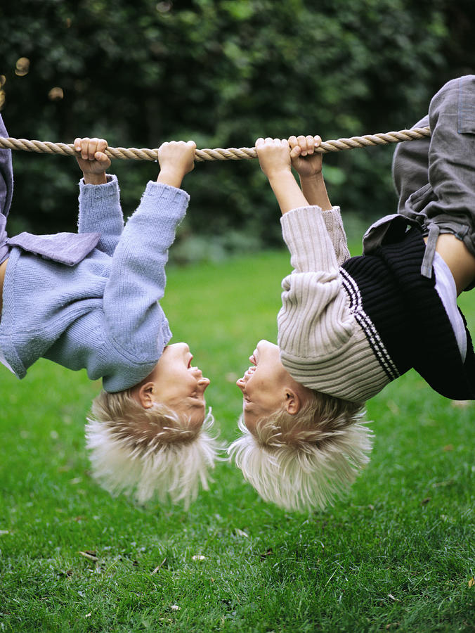 Twin brothers (6-8) hanging from rope, upside down, outdoors Photograph by David Trood