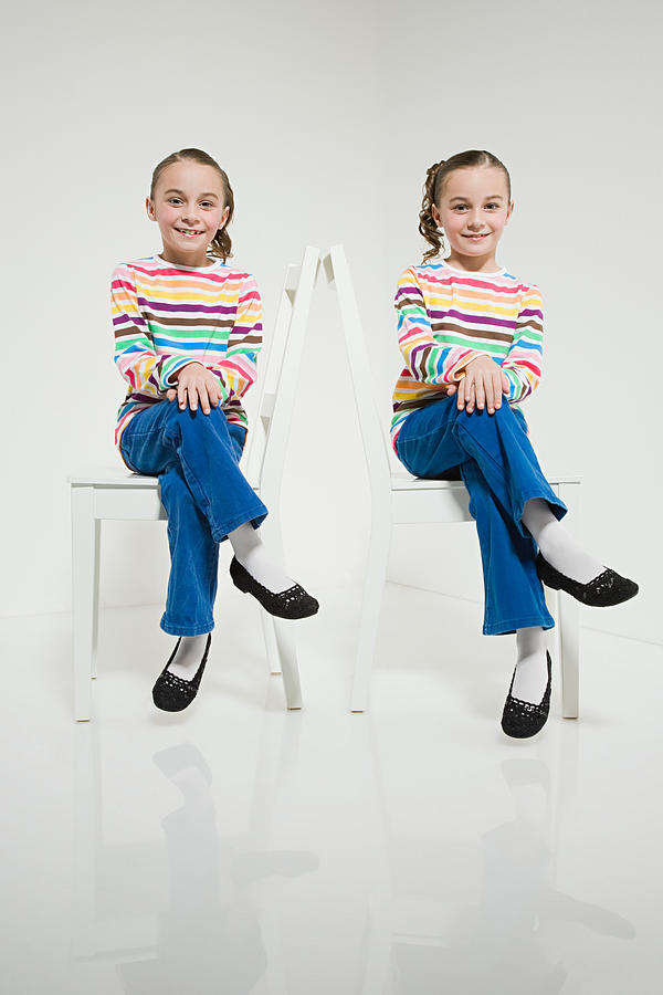 Twin sisters sitting on chairs Photograph by Image Source