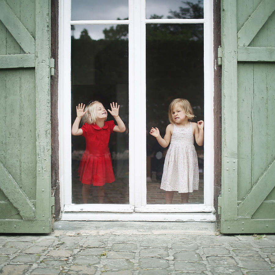 Two 3 years old twins girls posing behind a window Photograph by Catherine Delahaye
