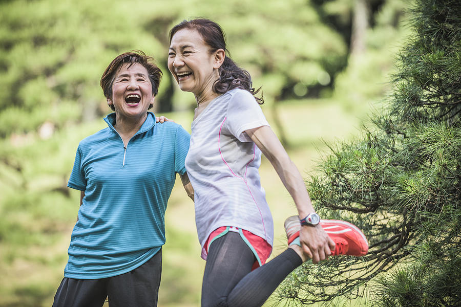 Two active Japanese women laughing, one stretching leg Photograph by JohnnyGreig