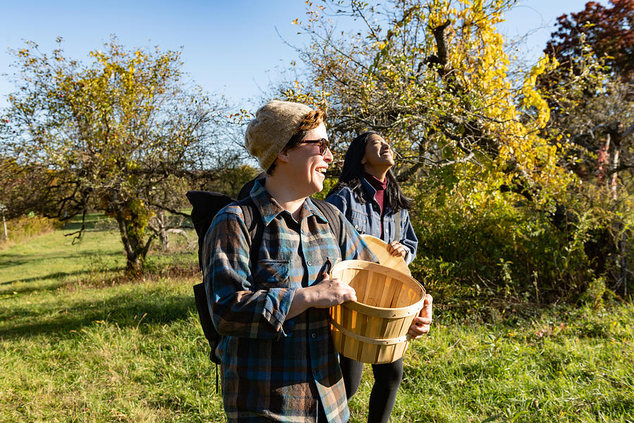 Two Adult Friends in 30s Walking Together with Apple Picking Baskets on a New York Farm in Autumn Photograph by Boogich