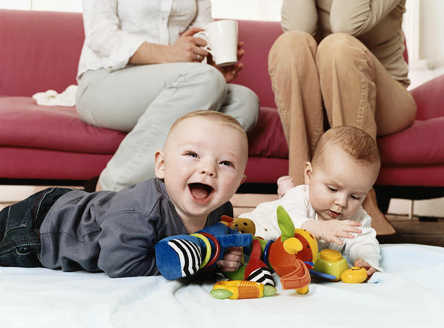 Two Babies Playing with Cuddly Toys on a Living Room Floor Photograph by Digital Vision.