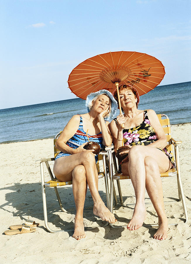 Two Bored Looking Women Sitting on Chairs Under a Parasol Photograph by Digital Vision.