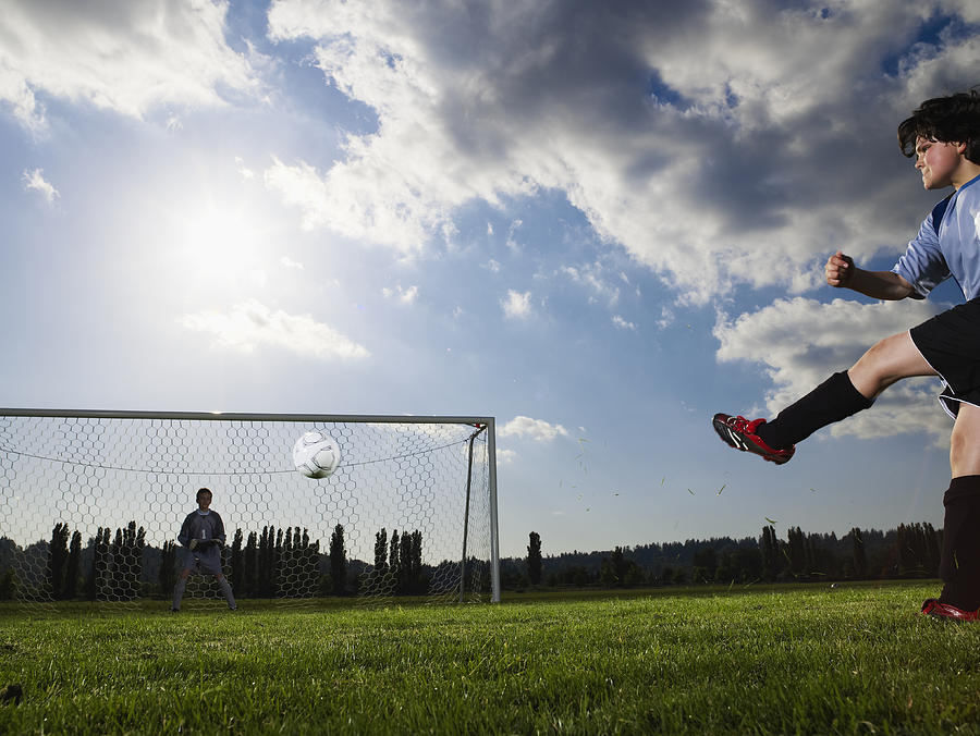 Two boys (10-13) playing football, one kicking, other in goal Photograph by Thomas Barwick