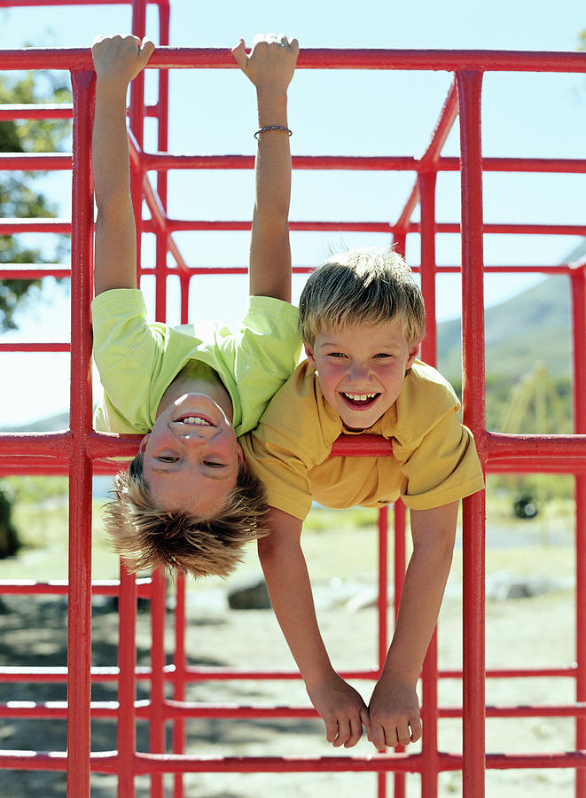 Two boys (9-11) hanging on bars in playground, smiling, portrait Photograph by Digital Vision