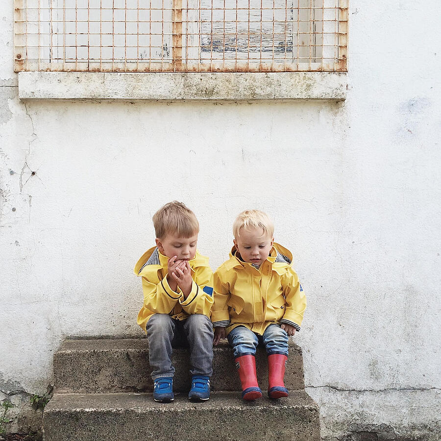 Two boys sitting on step wearing raincoats Photograph by Hannahargyle