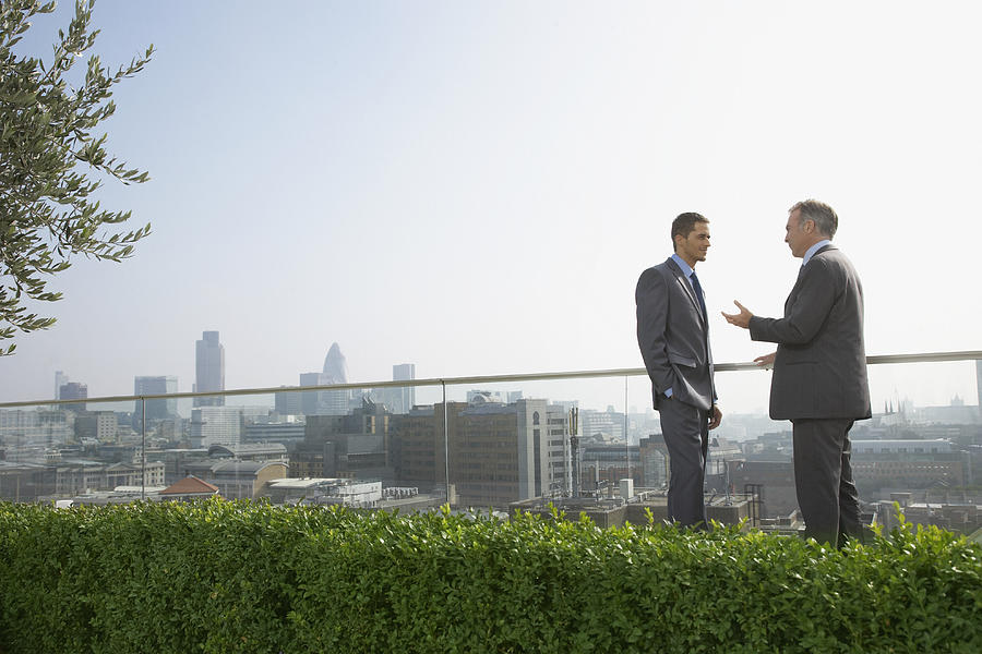 Two businessmen on rooftop talking, side view  Photograph by Justin Pumfrey