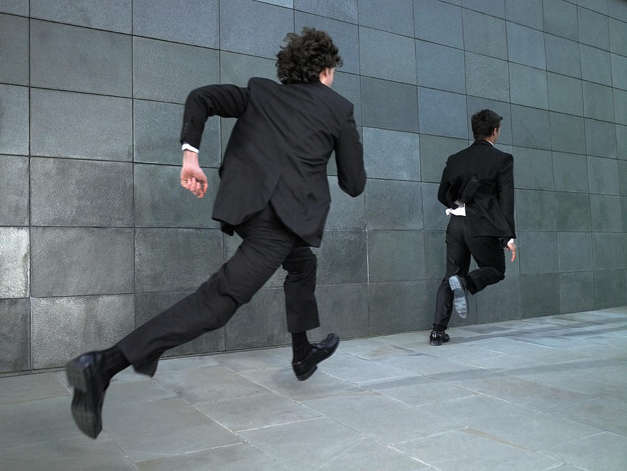Two businessmen running along street, rear view Photograph by Michael Blann
