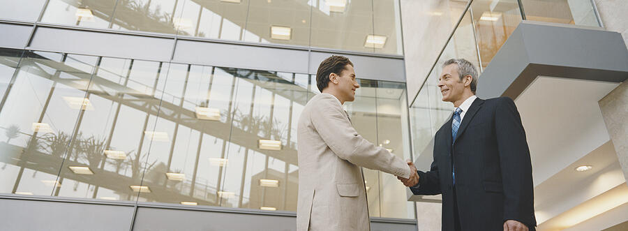 Two Businessmen Shaking Hands Standing Outside an Office Building Photograph by Digital Vision.