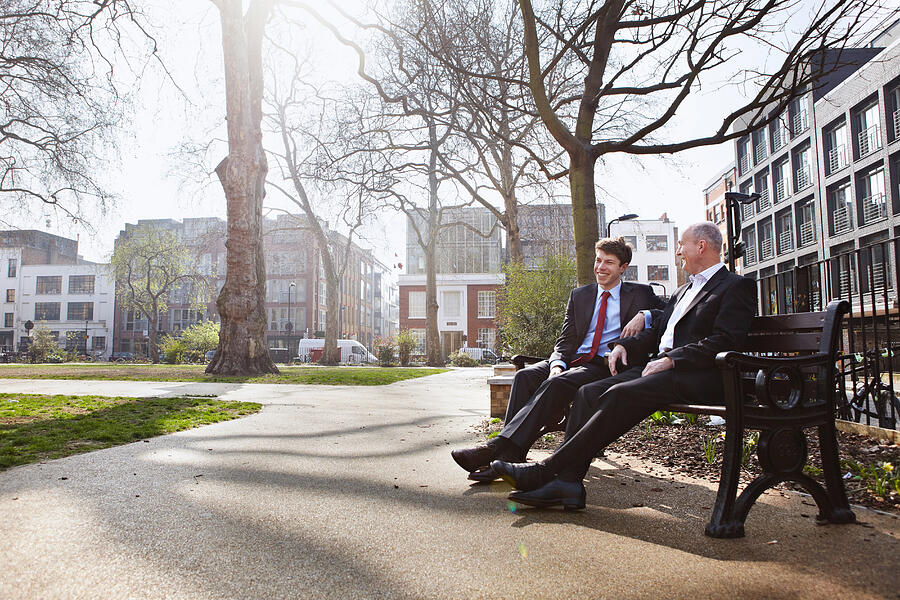 Two businessmen sitting on park bench Photograph by Liam Norris