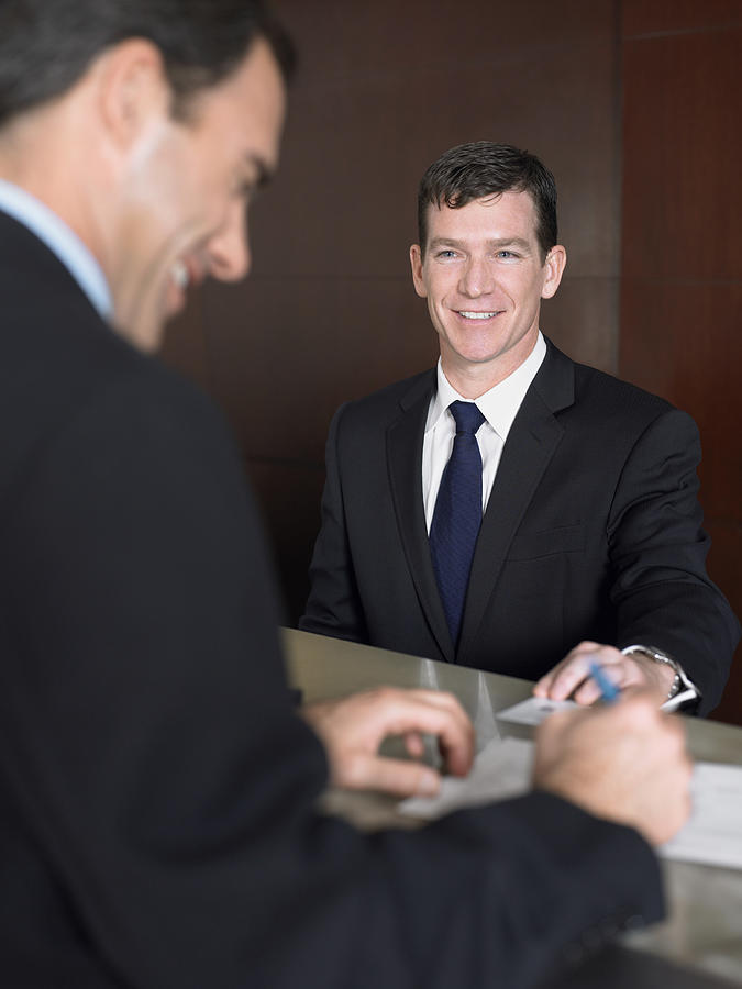 Two Businessmen Stand Smiling at a Reception Desk Signing Documents Photograph by Digital Vision.