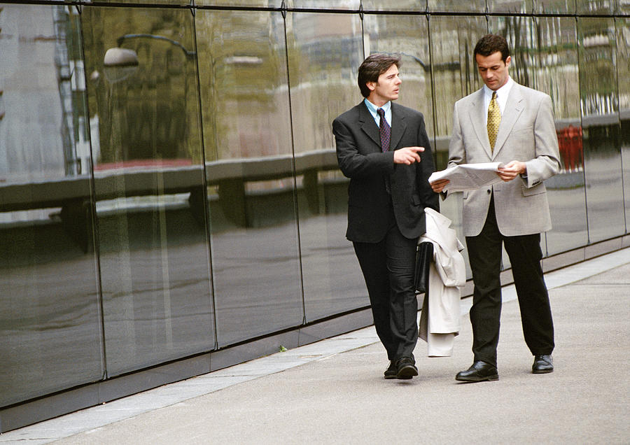 Two businessmen walking along sidewalk in front of building Photograph by Eric Audras