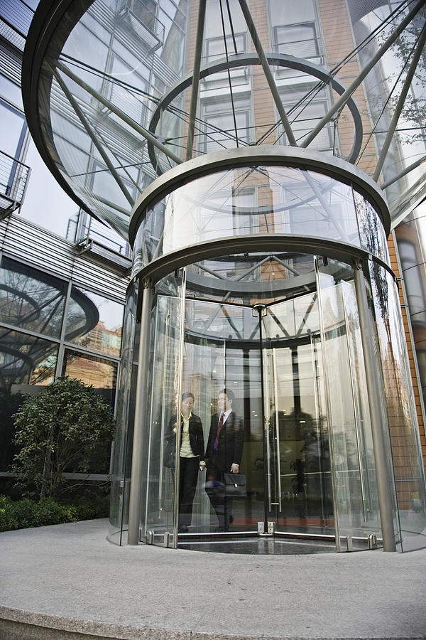 Two businesspeople standing behind revolving door Photograph by Kim Steele