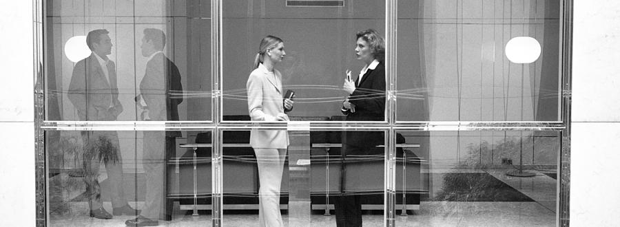 Two businesswomen behind large glass window, B&W Photograph by Teo Lannie