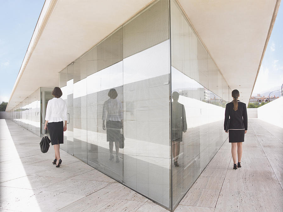Two businesswomen walking either side of building, rear view Photograph by Tom Merton