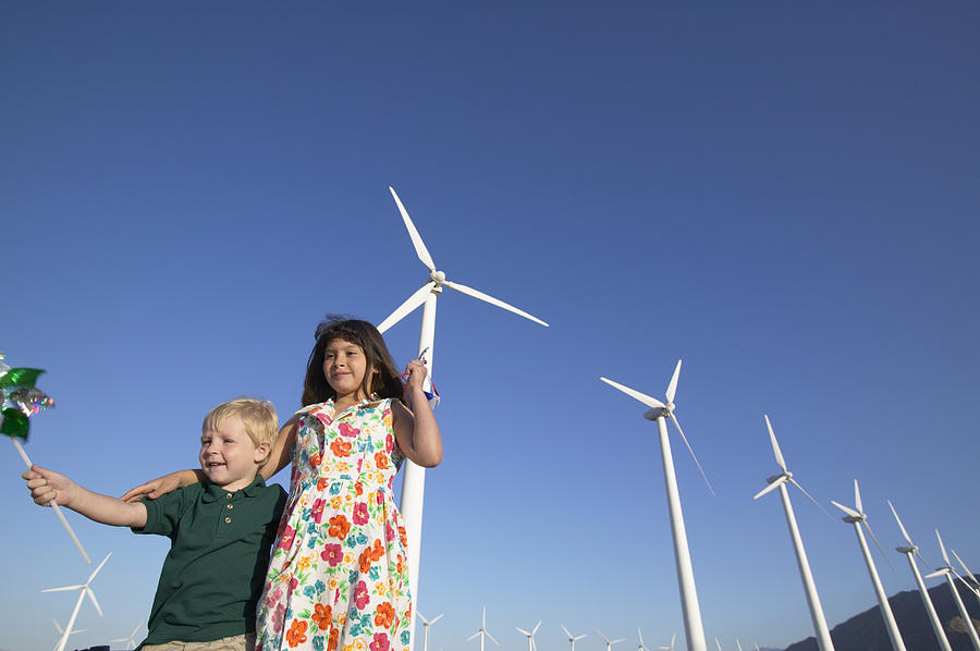 Two Children Holding Pinwheels and Standing in a Wind Farm Photograph by Digital Vision.
